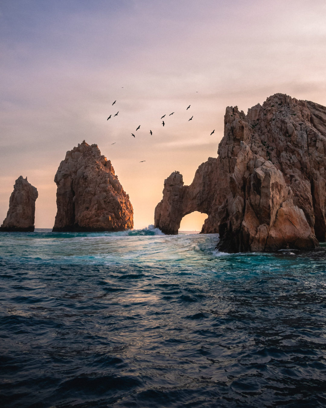 A orange and purple sunset behind the arch of Cabo San Lucas off the Pacific coast of Mexico near Cabo.