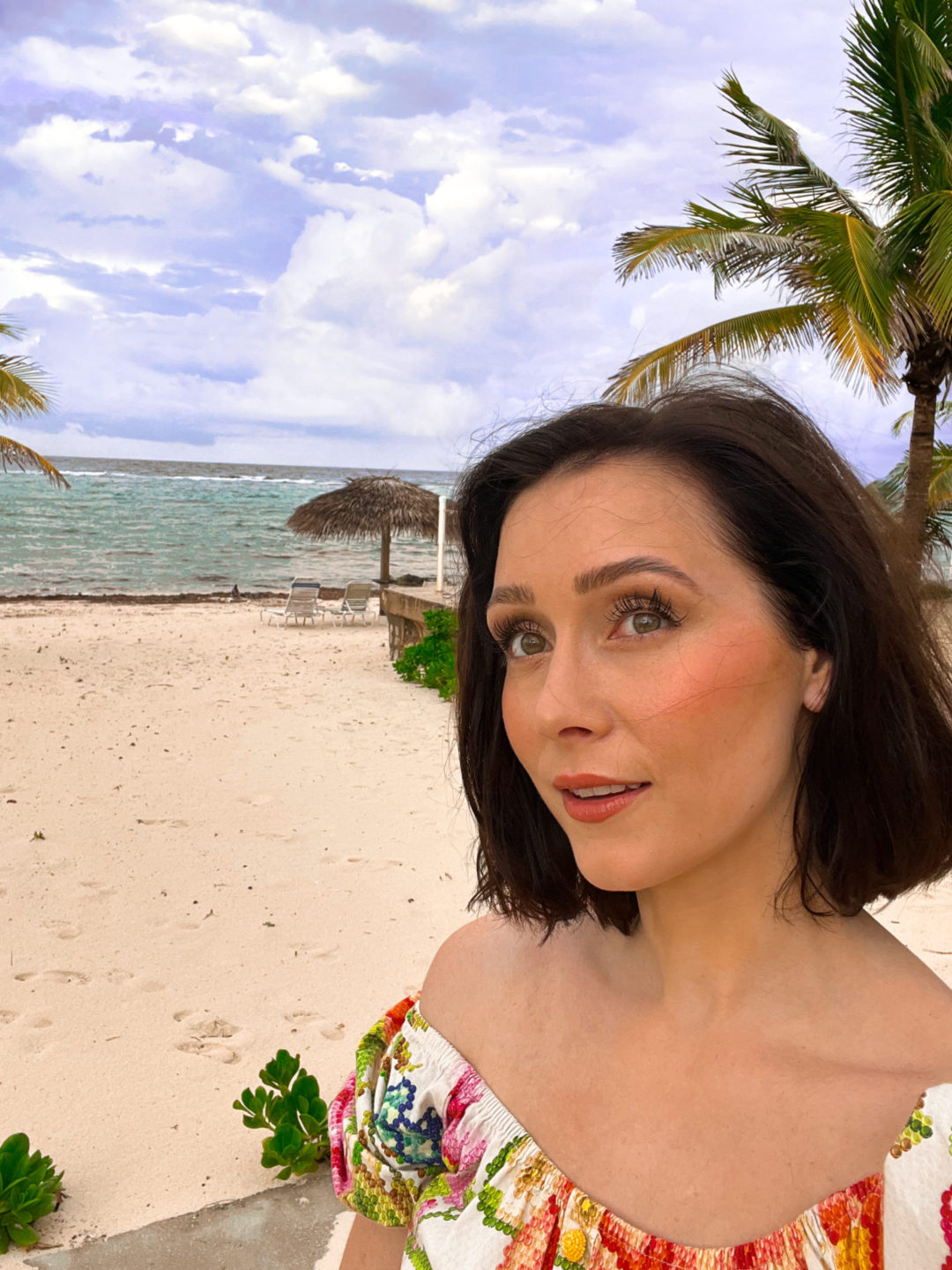 Travel Blogger Jordan Gassner taking.a selfie on a beach in Cayman Islands while wearing a Farm Rio Vintage Floral Dress