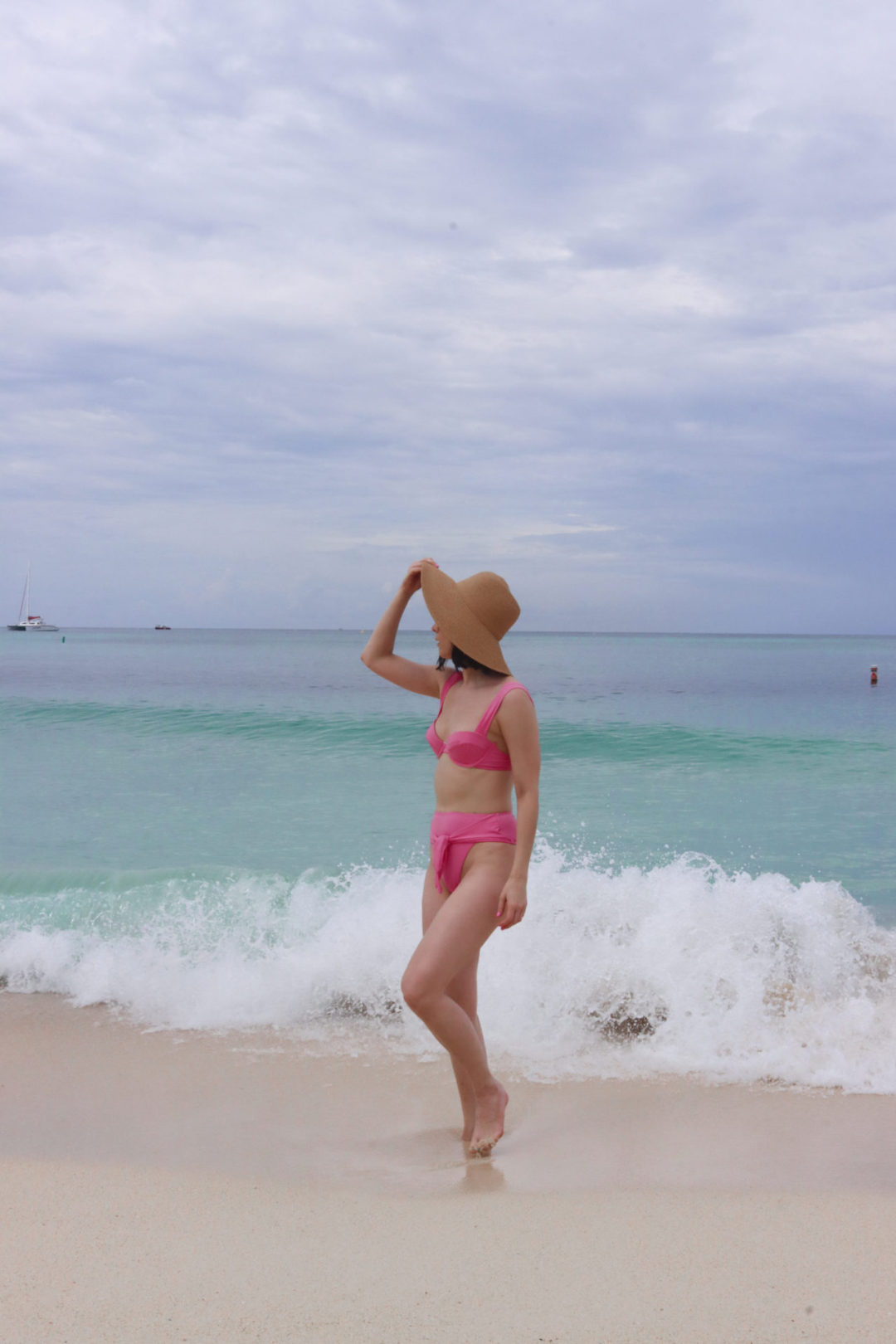 Travel Blogger Jordan Gassner looking out at the ocean under the wide brim of a straw hat on Governor's Beach in the Cayman Islands
