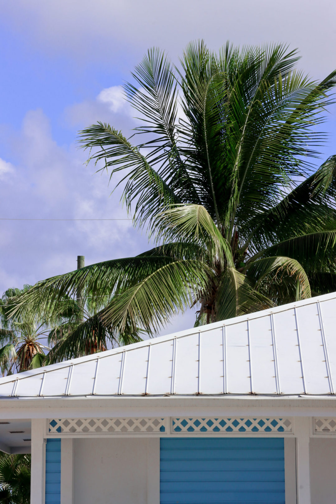 The roof of a white and blue Cayman Islands style building sitting under a palm tree and a blue sky at Rum Point on Grand Cayman Island