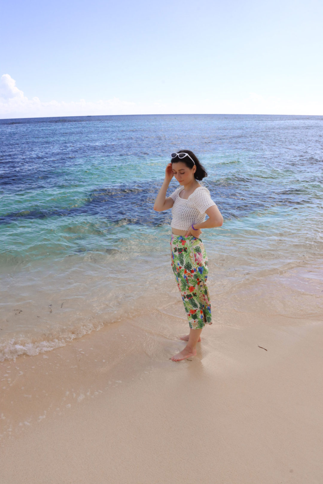 Travel Blogger Jordan Gassner looking down at the sand and standing near the water on Spotts Beach in the Cayman Islands