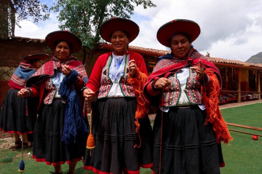 Three Peruvian women smiling while showing off their weaving equipment at El Centro De Textiles Tradicionales Del Cusco in Chinchero, Peru