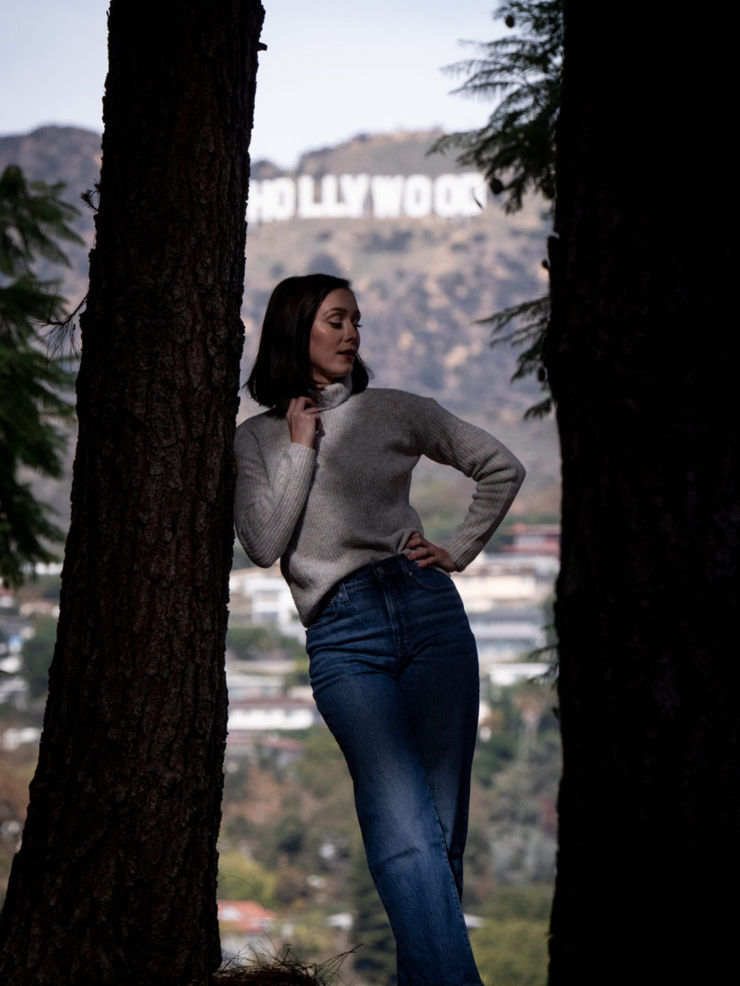 Travel Blogger Jordan Gassner leaning against a tree and looking down at Barnsdall Art Park with the Hollywood Sign in the background