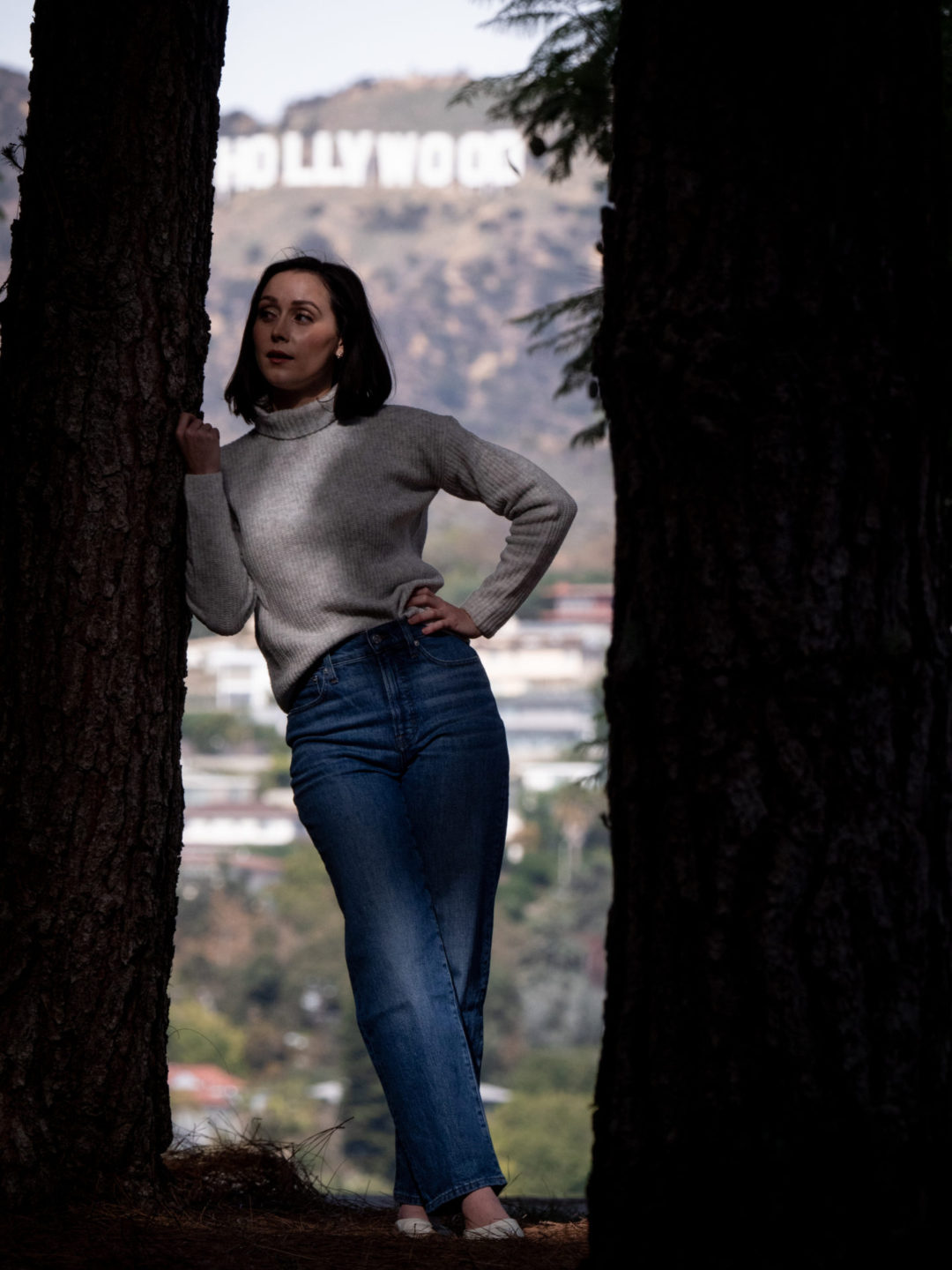 Travel Blogger Jordan Gassner leaning against a tree at Barnsdall Art Park with the Hollywood Sign in the background