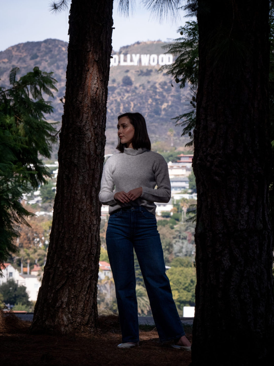 Travel Blogger Jordan Gassner standing in between two trees at the Los Angeles Barnsdall Art Park with the Hollywood Sign in the background