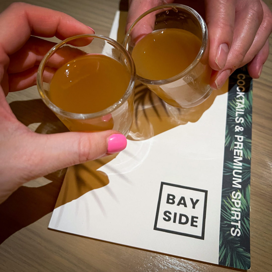 Travel Blogger Jordan Gassner and her partner holding complimentary Fermented Pineapple Shots from Bayside restaurant in Cayman Islands