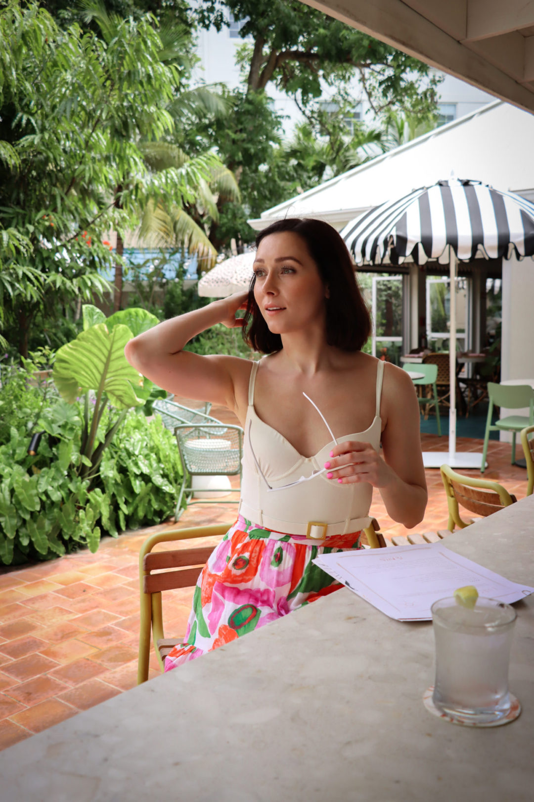 Travel Blogger Jordan Gassner pushing back her hair and holding sunglasses at Ms. Piper's Restaurant in Cayman Islands