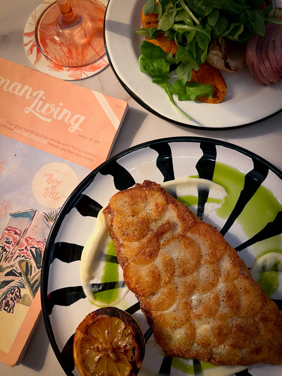 Potato-Crusted Branzino and a Side Salad near a pink menu with the words "Cayman Living" at Ms. Piper's Restaurant in Cayman Islands