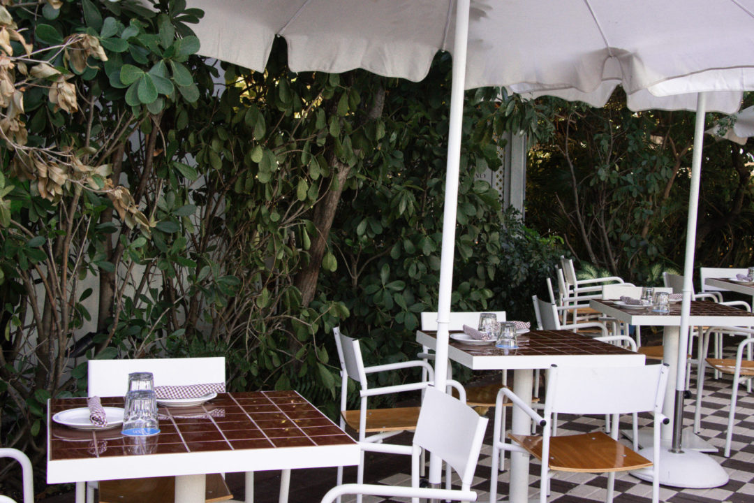 A series of brown and white tiled tables with white chairs and umbrellas at Paradise Pizza on Grand Cayman Island