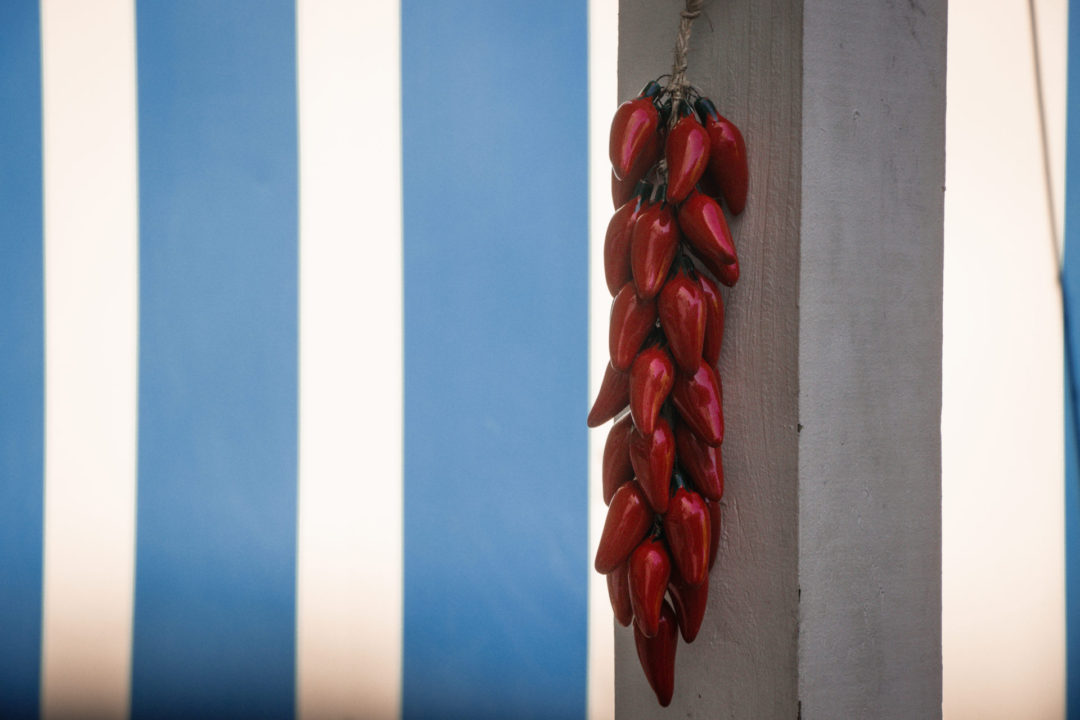 A series of red peppers hanging from a white post in front of a blue and white striped trailer at Paradise Pizza on Grand Cayman Island