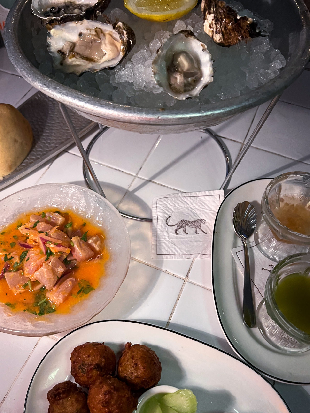 A tray of oysters and sauces next to the Aji Ceviche, Mustard Green Fritter and a Leopard Branded Napkin at Tillie's Restaurant in Cayman Islands