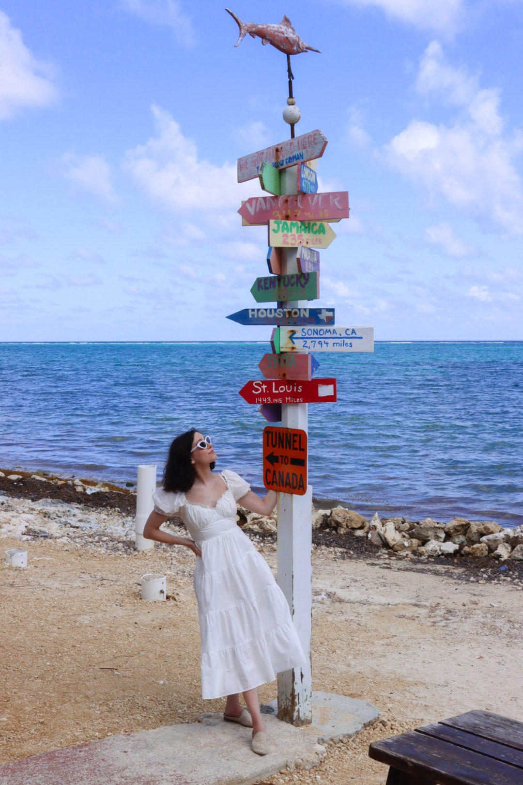 Travel Blogger Jordan Gassner looking up at a colorful directional sign-post on the east end beach of Grand Cayman Island