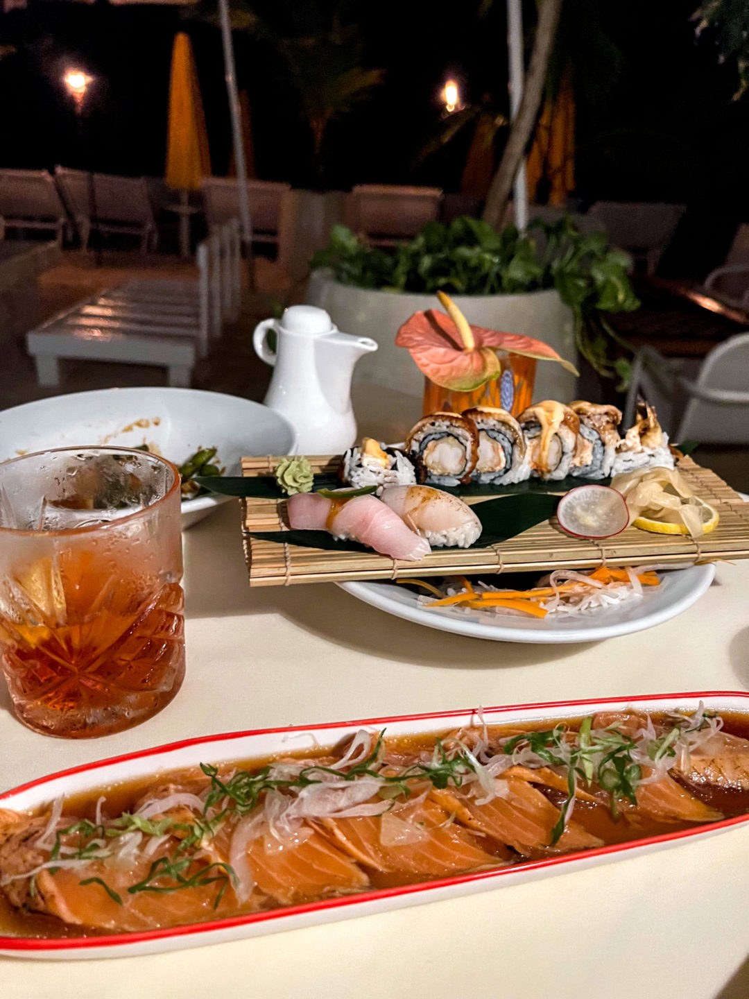 A negroni and two trays of colorful sushi on a table near the beach at Yashinoki Restaurant in Cayman Islands