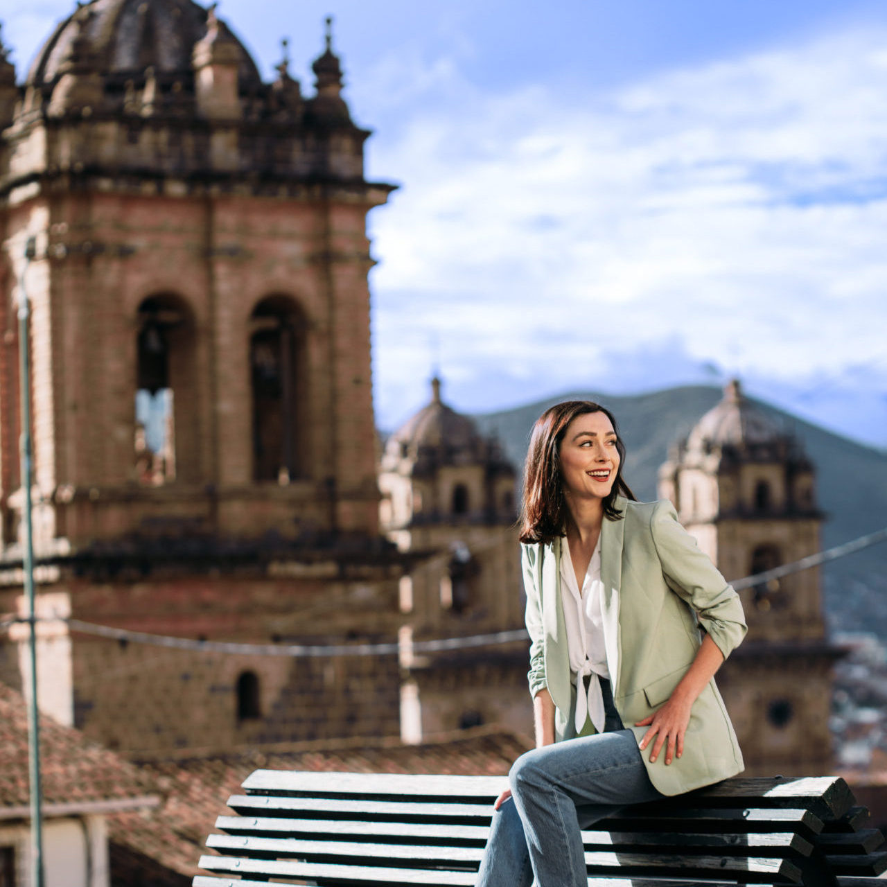 Travel Blogger Jordan Gassner leaning forward and smiling while sitting on a bench in Cusco, Peru's Plaza Tricentenario