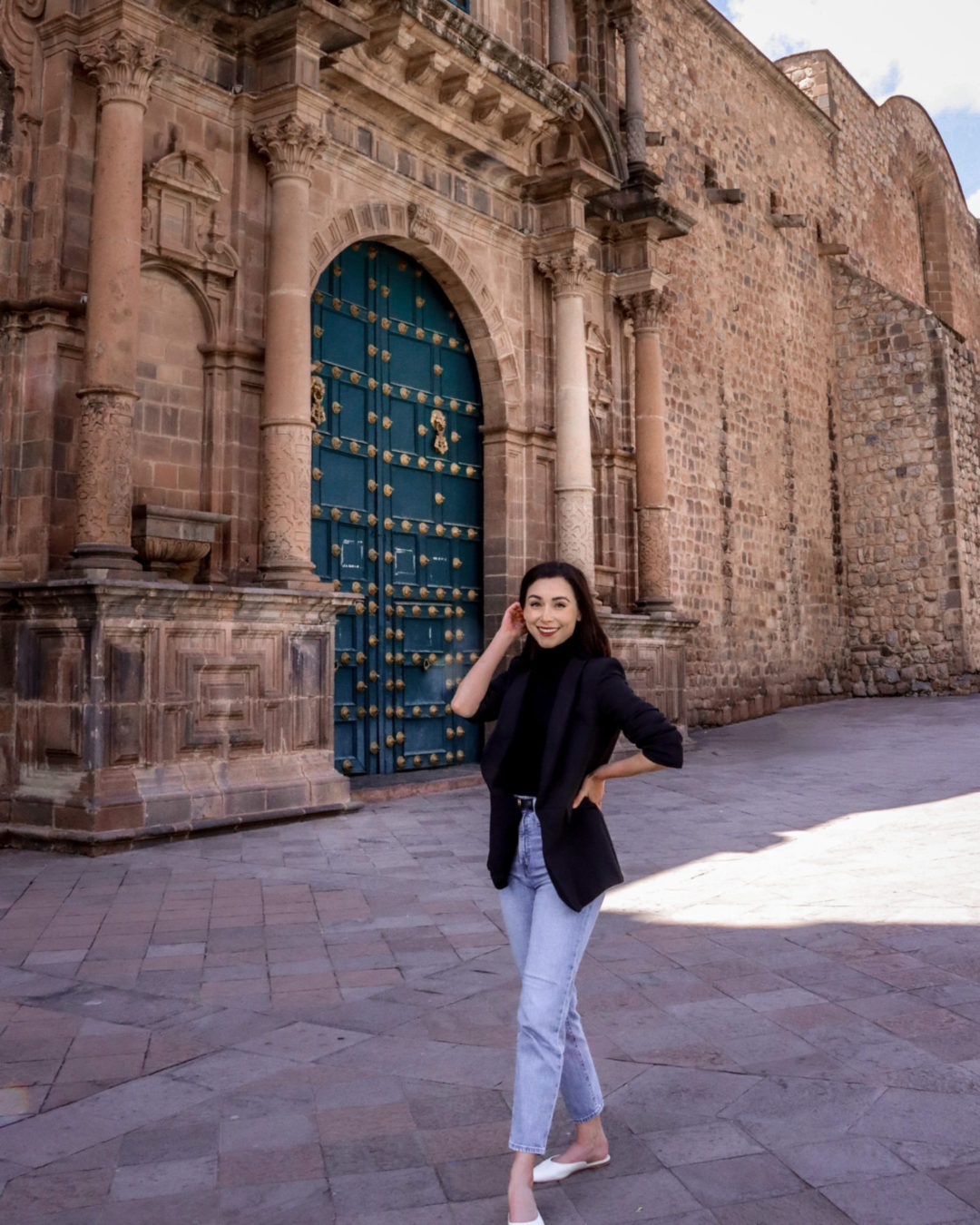 Travel Blogger Jordan Gassner pushing her hair back in front of the green gate at Convento La Merced in Cusco, Peru