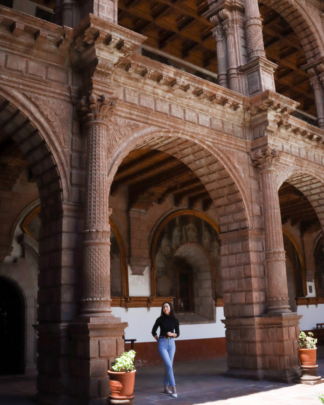 Travel Blogger Jordan Gassner dwarfed by the large two-story arched porticoes in Covento La Merced in Cusco, Peru