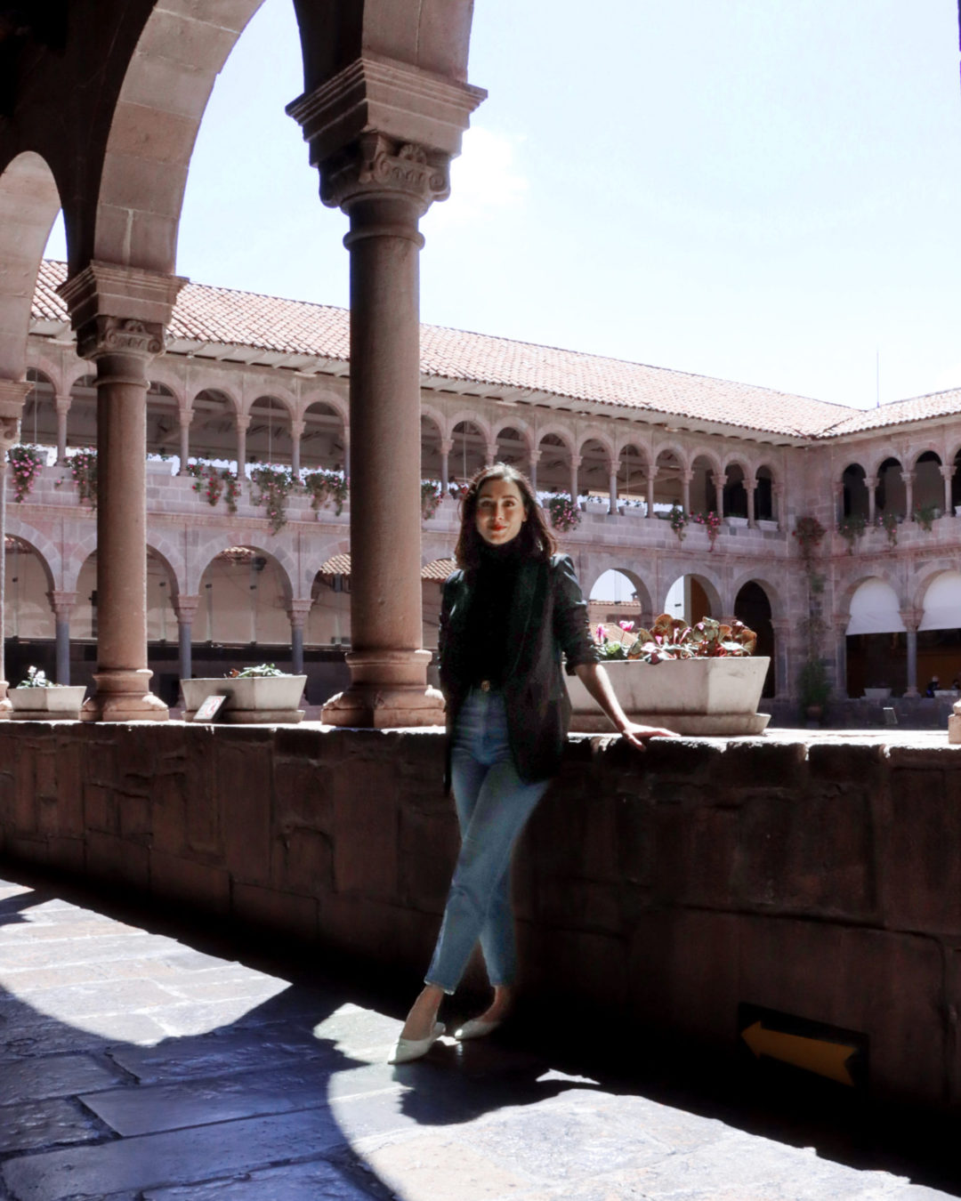 Travel Blogger Jordan Gassner leaning against a stone fence surrounding the central courtyard at Qoricancha Temple in Cusco, Peru
