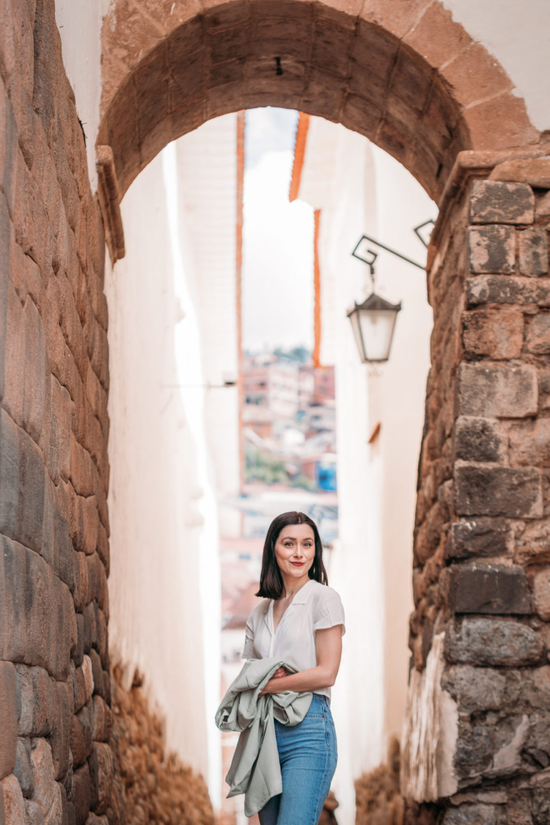 Travel Blogger Jordan Gassner standing and holding her jacket in the archway at Calle Siete Culebras in Cusco, Peru.