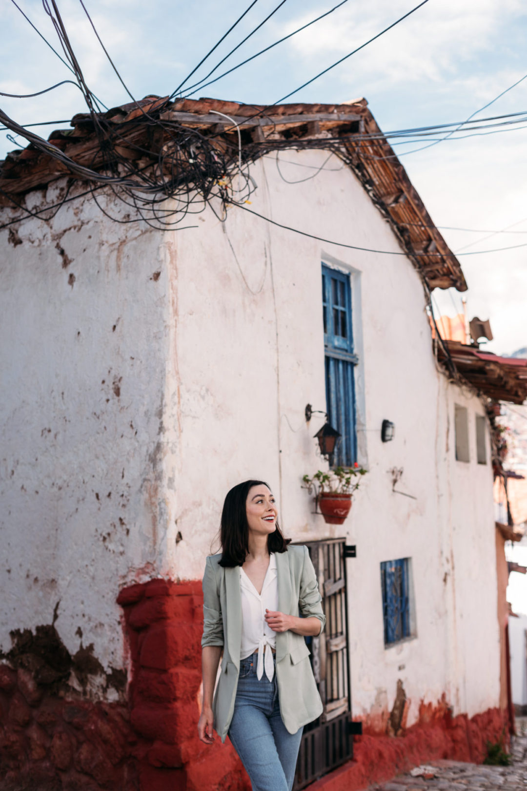 Travel Blogger Jordan Gassner walking near a white stucco building with blue windows and red bricks in San Blas in Cusco, Peru