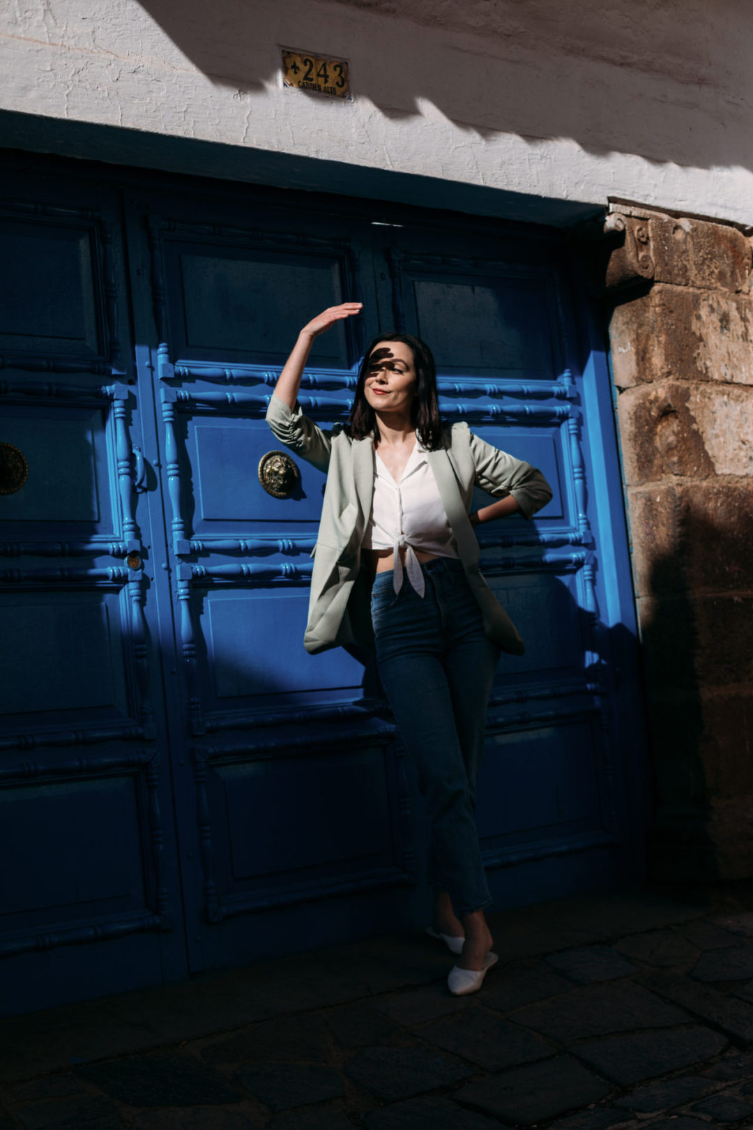 Travel Blogger Jordan Gassner shielding her eyes while standing in front of a blue door with large knobs in San Blas, Cusco, Peru