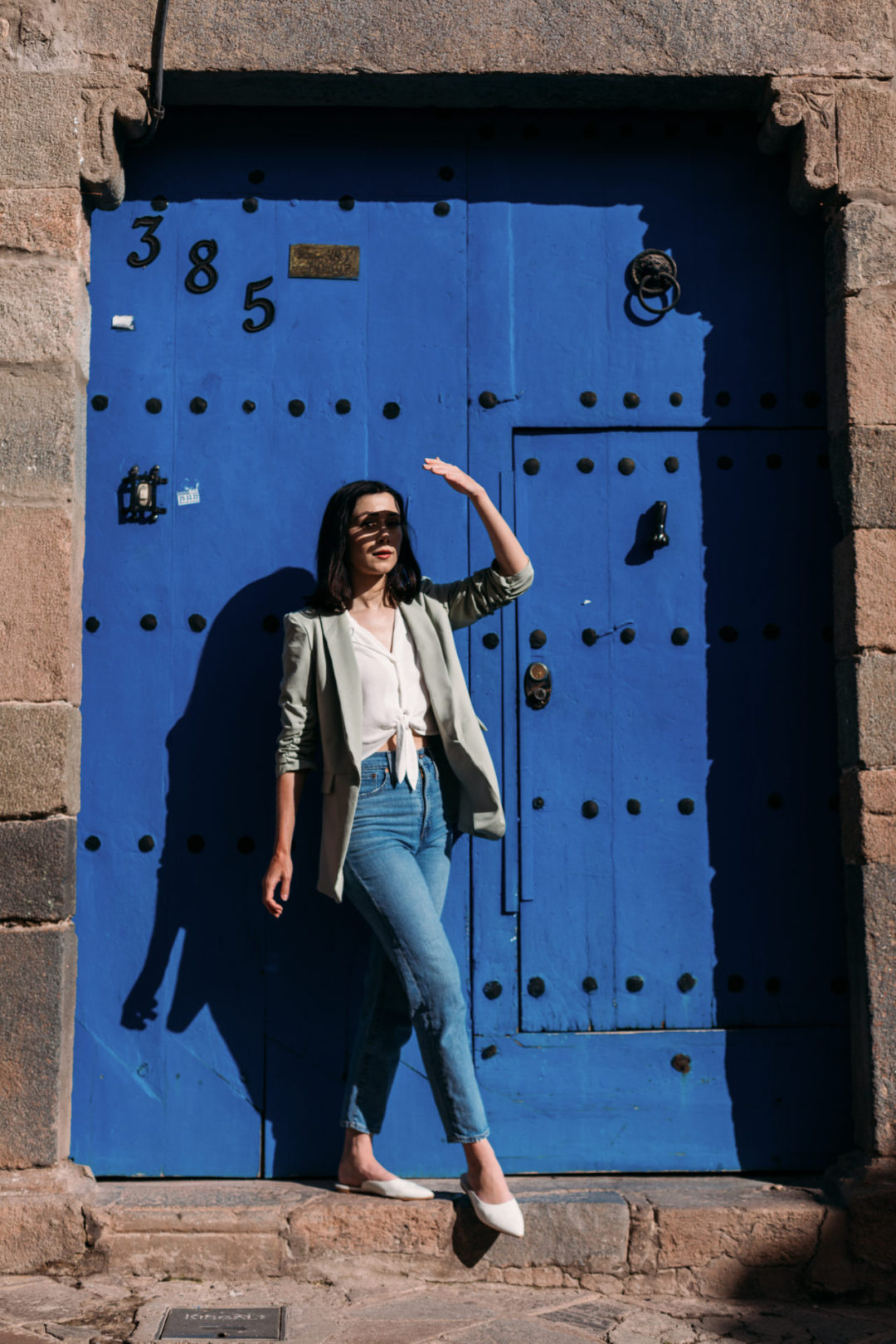 Travel Blogger Jordan Gassner shielding her eyes while standing in front of a blue door with large knobs in San Blas, Cusco, Peru