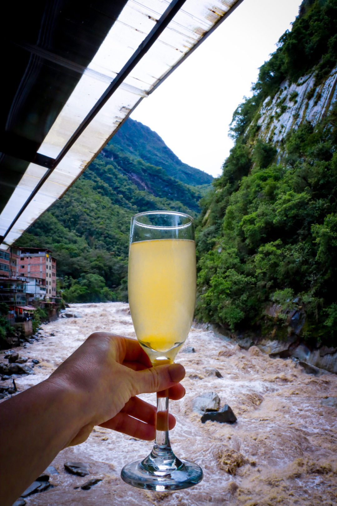 Travel Blogger Jordan Gassner holding up a mimosa from Mapacho Bar in Aguas Calientes, Peru 