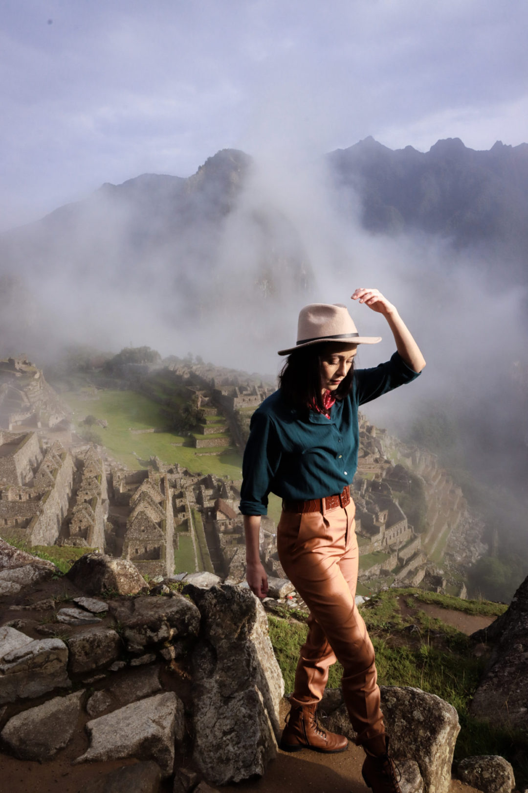 Travel Blogger Jordan Gassner looking down and reaching up to grab her hat on the steps of Machu Picchu's Lower Terrace in Peru