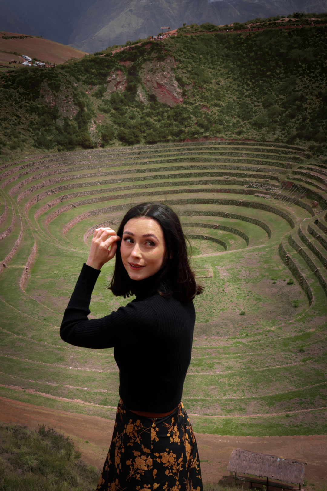 Travel Blogger Jordan Gassner brushing her hair back with her hand while standing at the top the Moray Archaeological Site in Peru