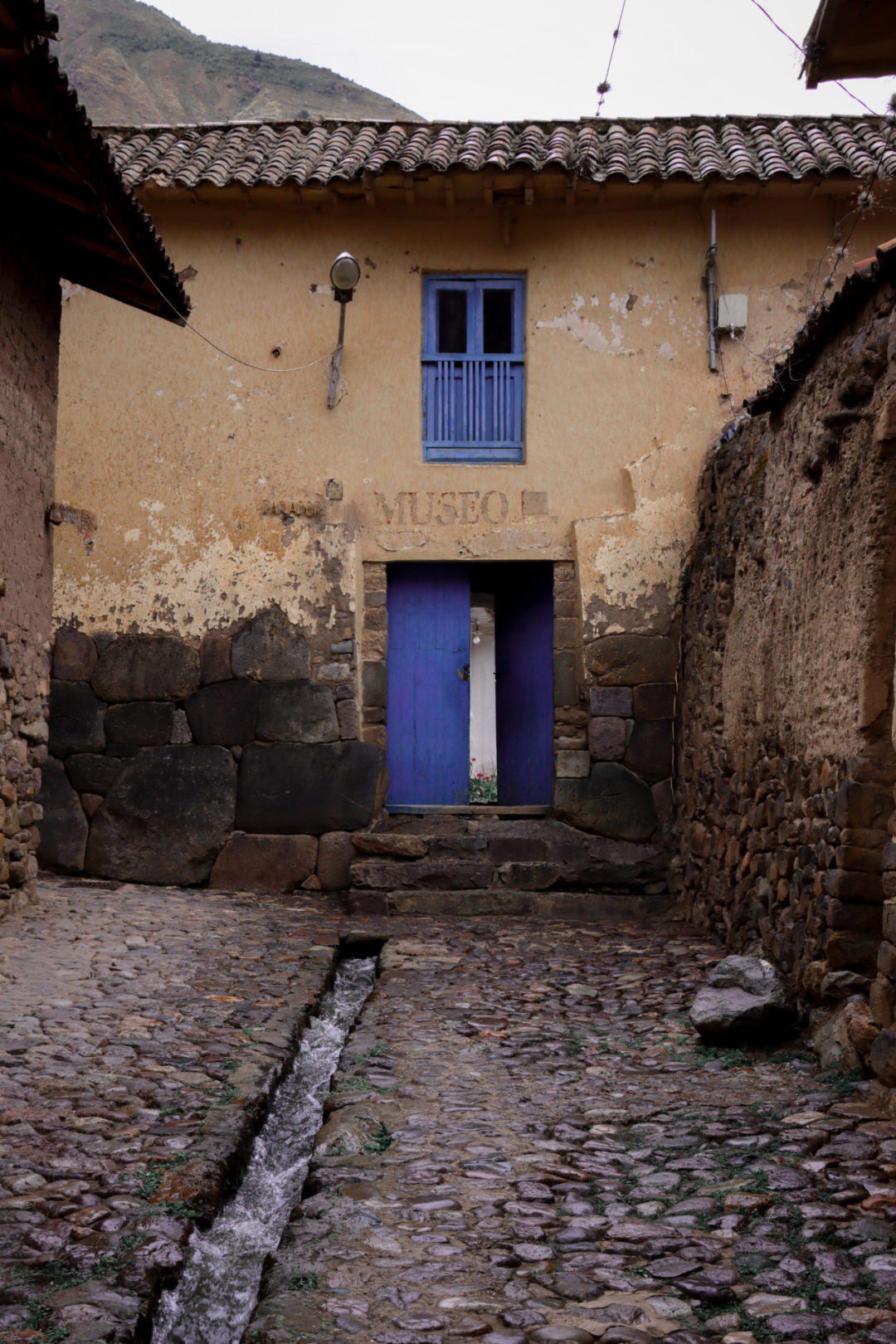 An old building in Ollantaytambo, Peru marked with the words "Museo" above a blue-painted set of wooden doors and beneath a blue balcony