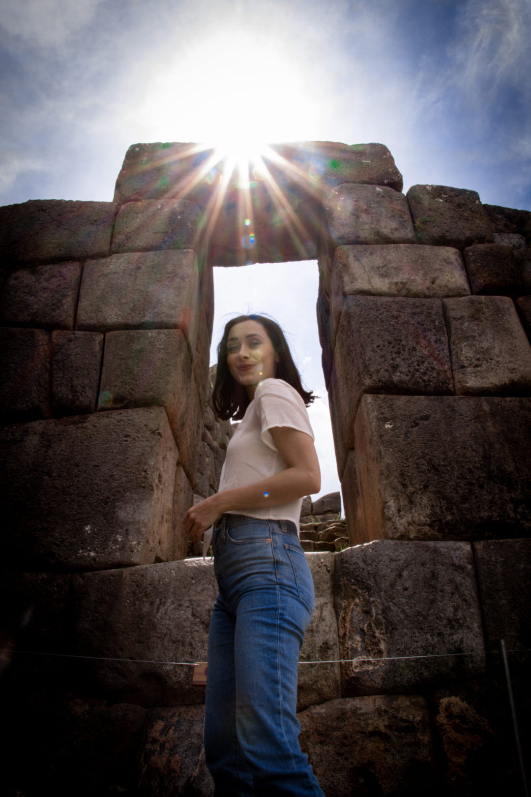 Travel Blogger Jordan Gassner standing under Sun Gate in Sacsayhuamán, Peru while the sun is crossing over the threshold overhead