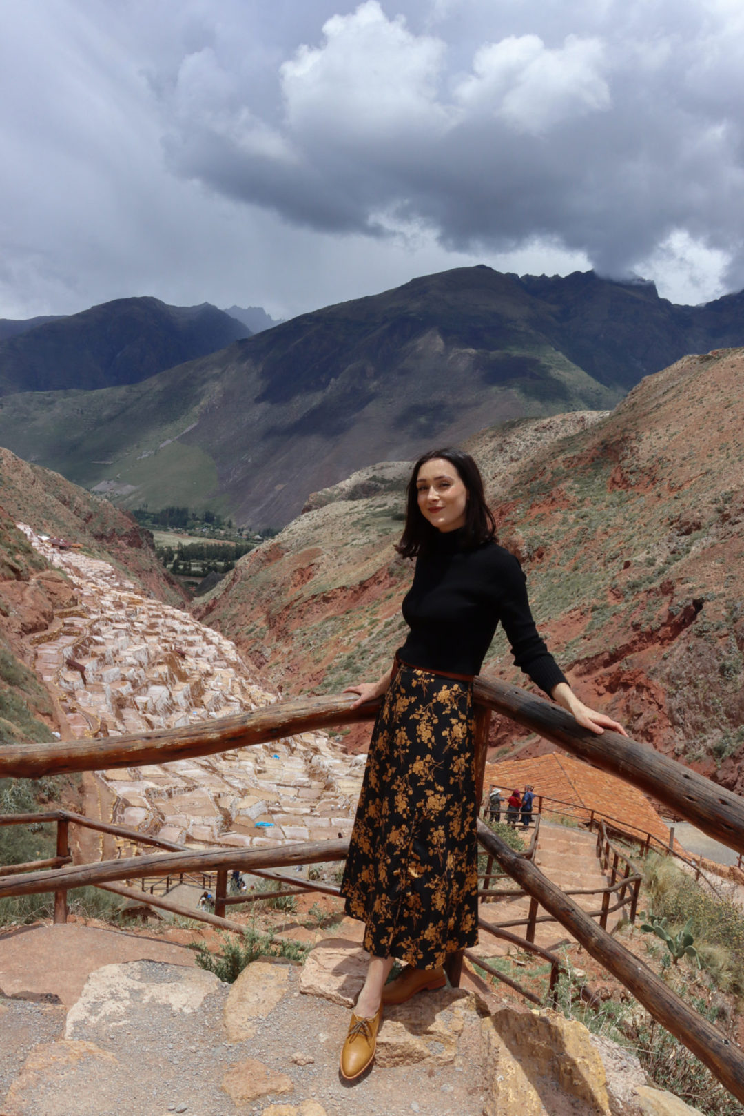 Travel Blogger Jordan Gassner smiling and leaning against a rail overlooking Salinas De Maras in Peru's Sacred Valley