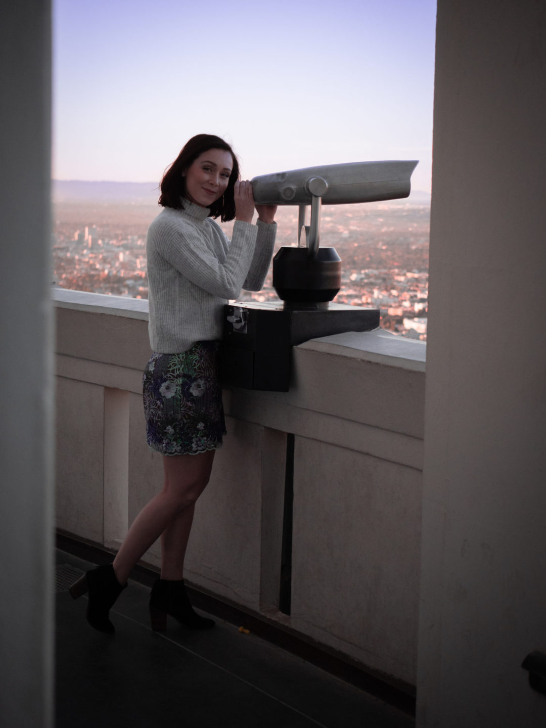 Travel Blogger Jordan Gassner smiling while holding a tower viewer under an archway of the Griffith Observatory in Los Angeles, California