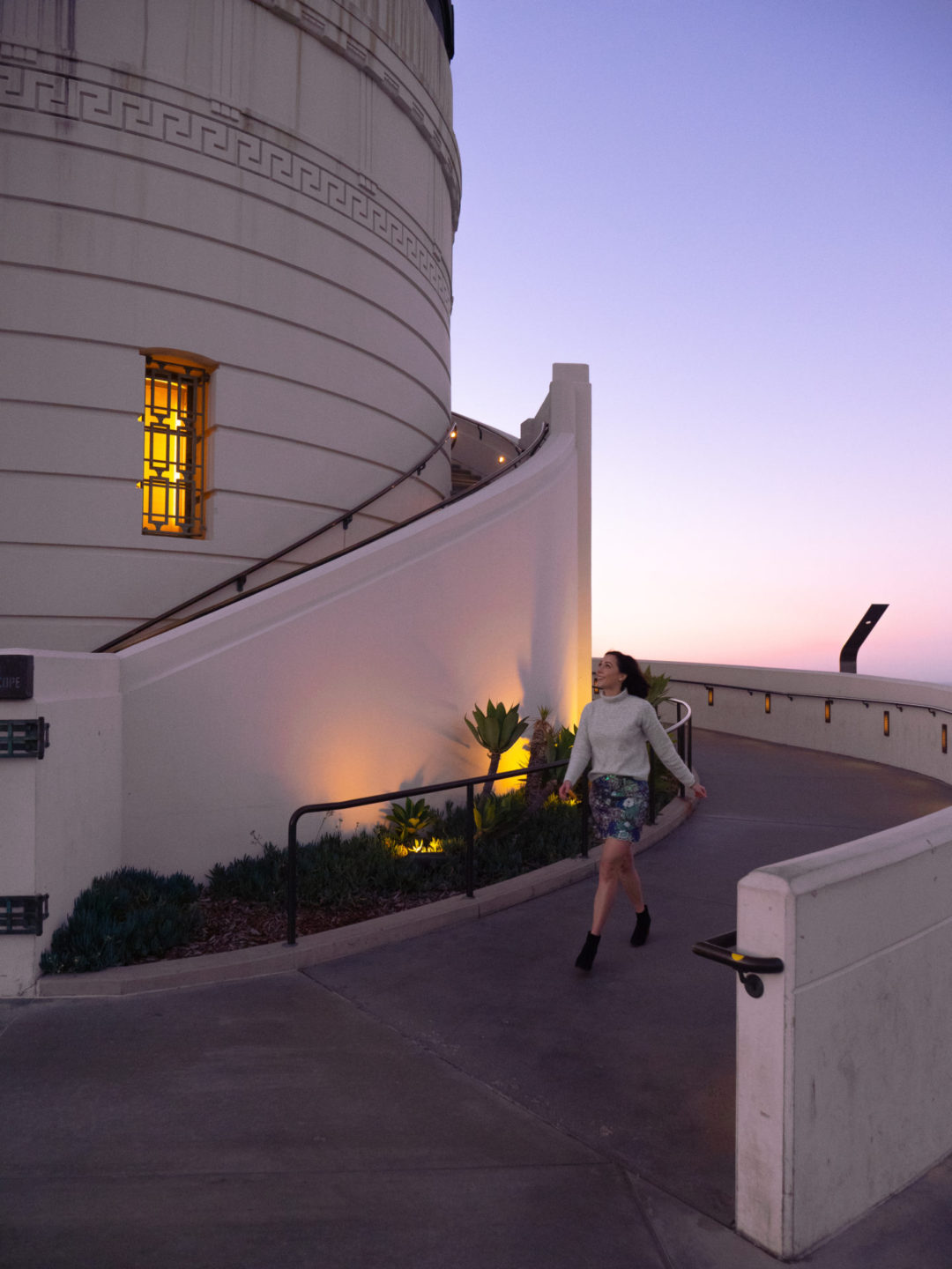 Travel Blogger Jordan Gassner smiling and walking down the ramp alongside Griffith Observatory's western rotunda in Los Angeles