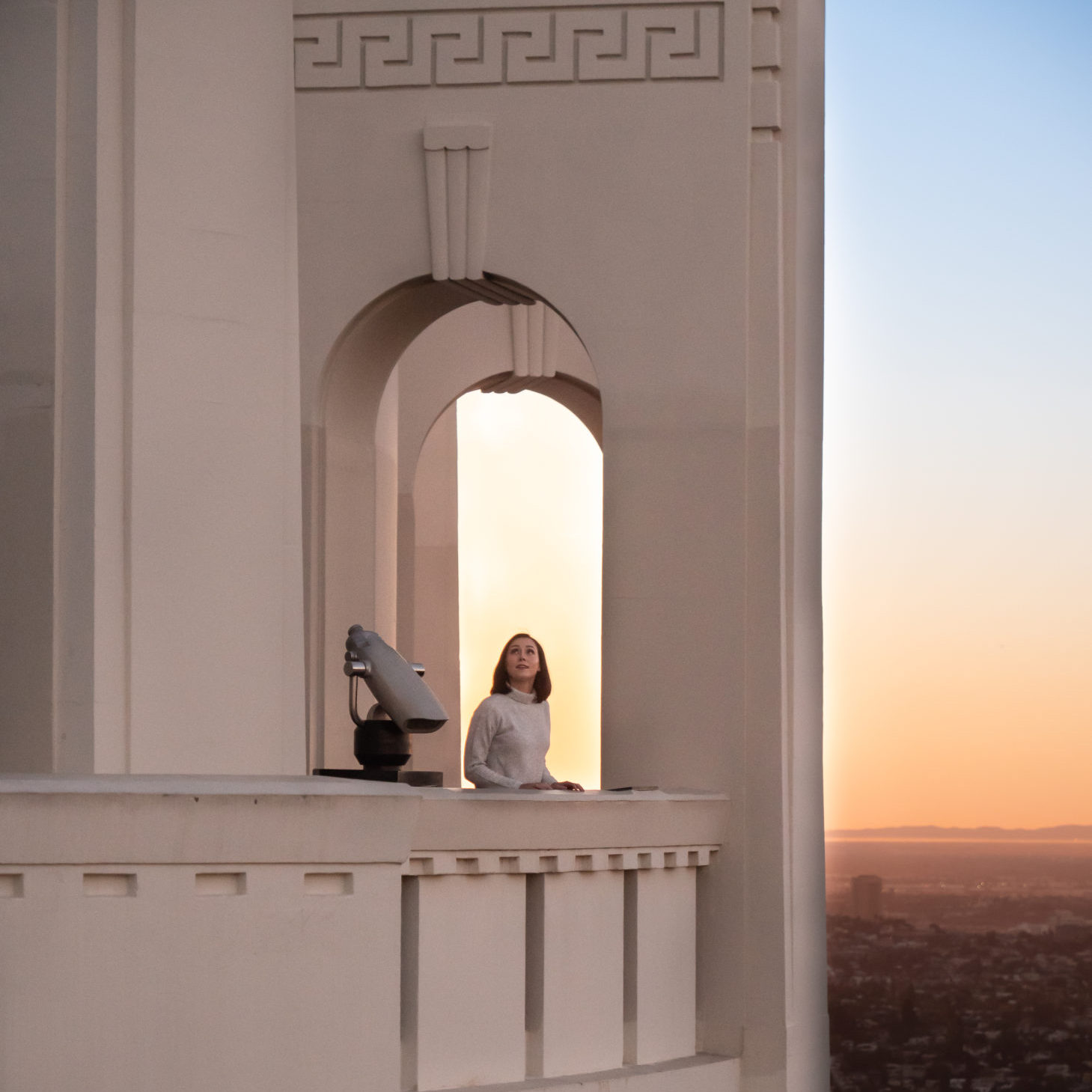 Travel Blogger Jordan Gassner standing next to a tower viewer at the back archway of Griffith Observatory overlooking LA