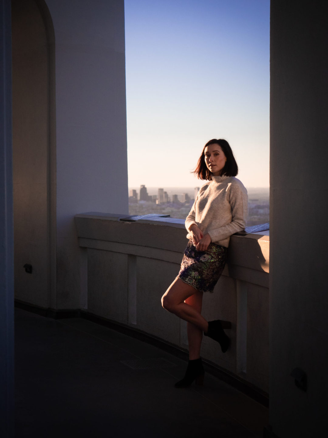 Travel Blogger Jordan Gassner leaning against the interior back archway of Griffith Observatory, the bottom of her foot resting against the wall