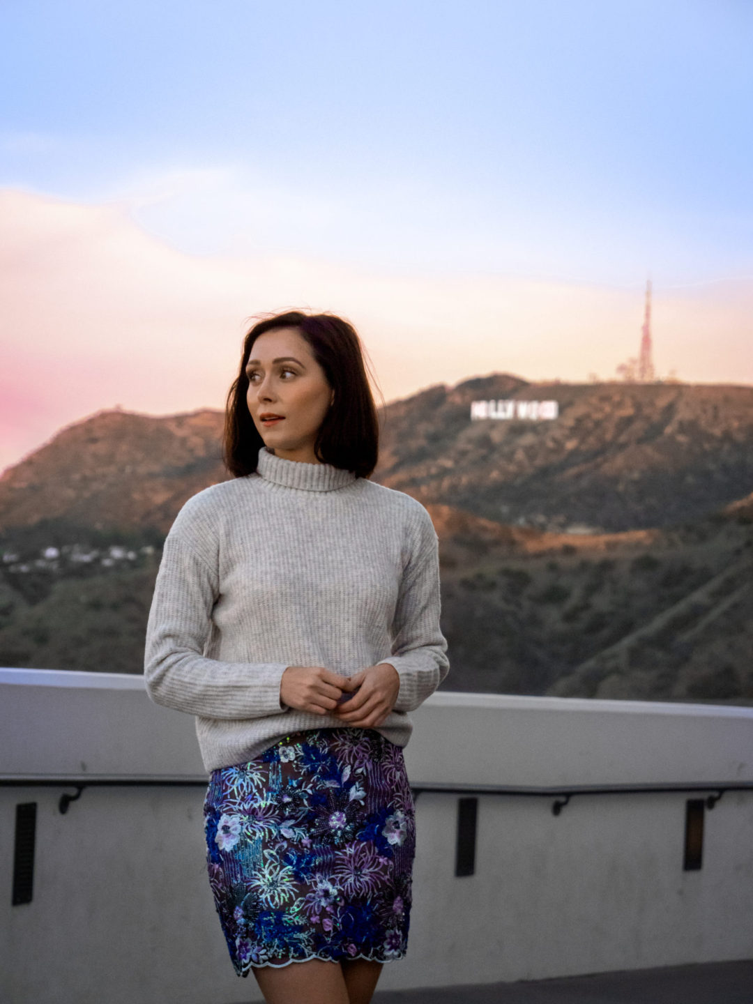 Travel Blogger Jordan Gassner bundled up during sunrise at the Griffith Observatory with the Hollywood Sign in the background