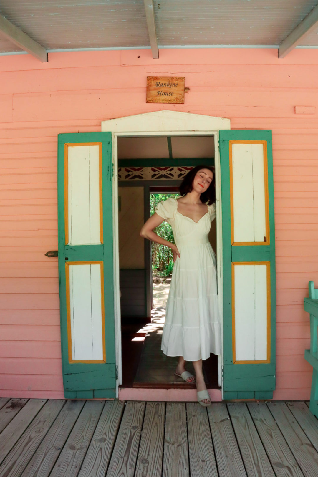 Travel Blogger Jordan Gassner standing in the doorway of a pink antique home in Cayman Islands