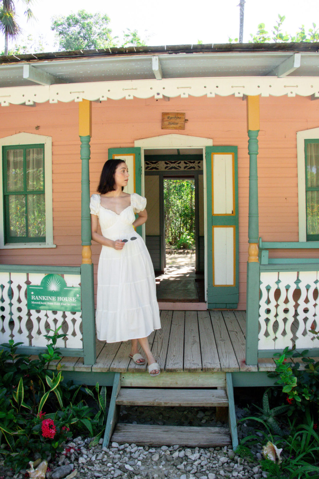 Travel Blogger Jordan Gassner standing on the porch of the pink Rankin Home at the Queen Elizabeth II Botanic Park in Cayman Islands