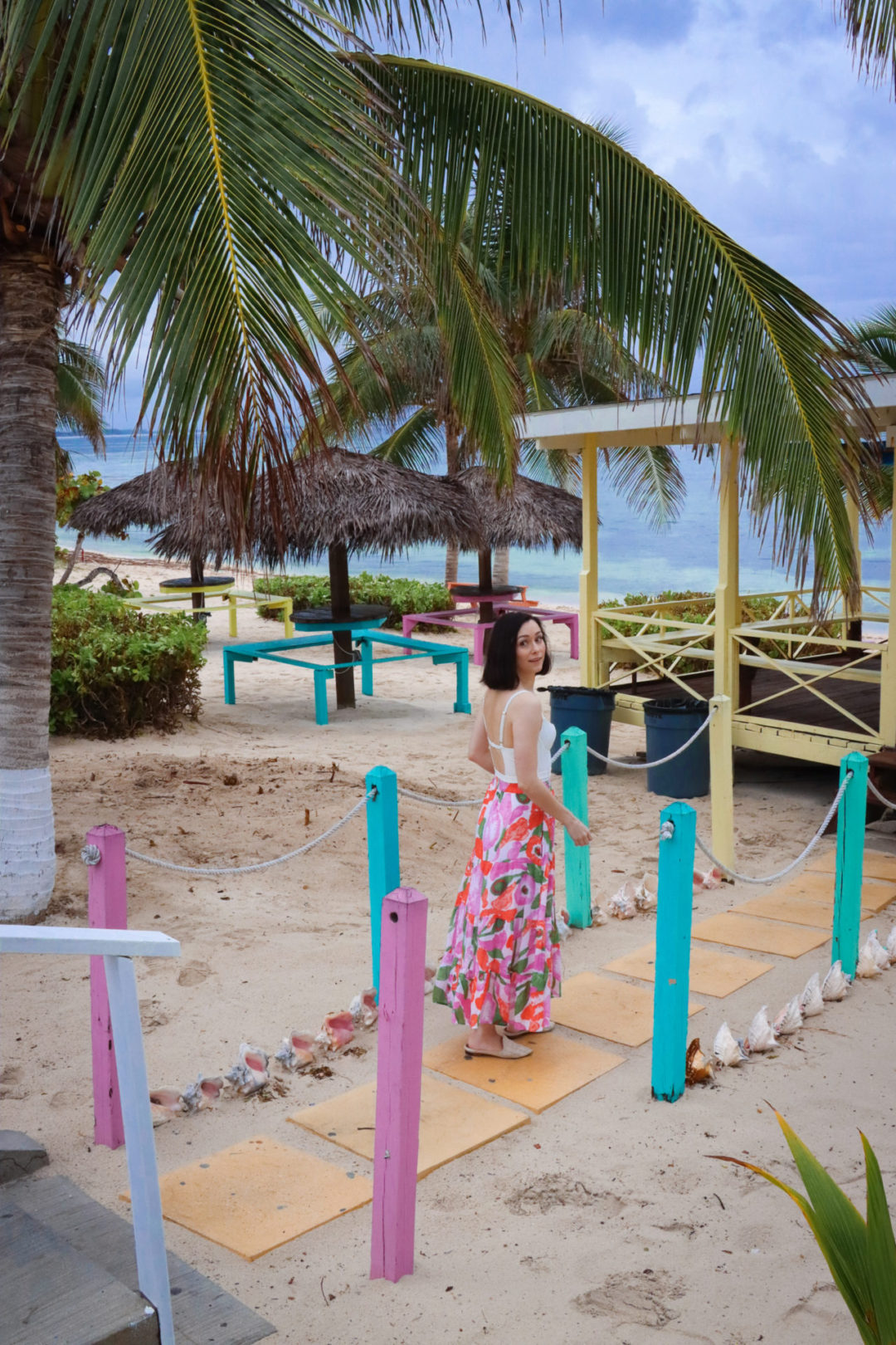 Travel Blogger Jordan Gassner looking over her shoulder and smiling on a colorful walkway in front of Grape Tree Cafe in Cayman Islands