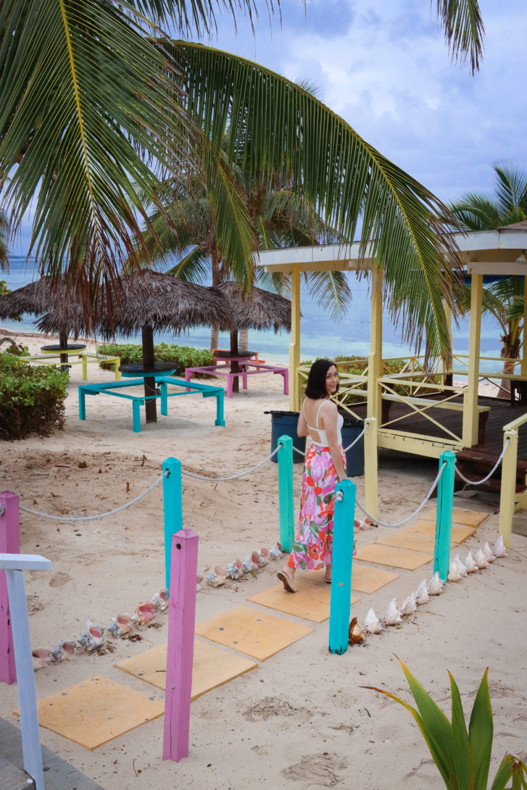 Travel Blogger Jordan Gassner looking over her shoulder while strolling along a colorful walkway in front of Grape Tree Cafe in Cayman Islands