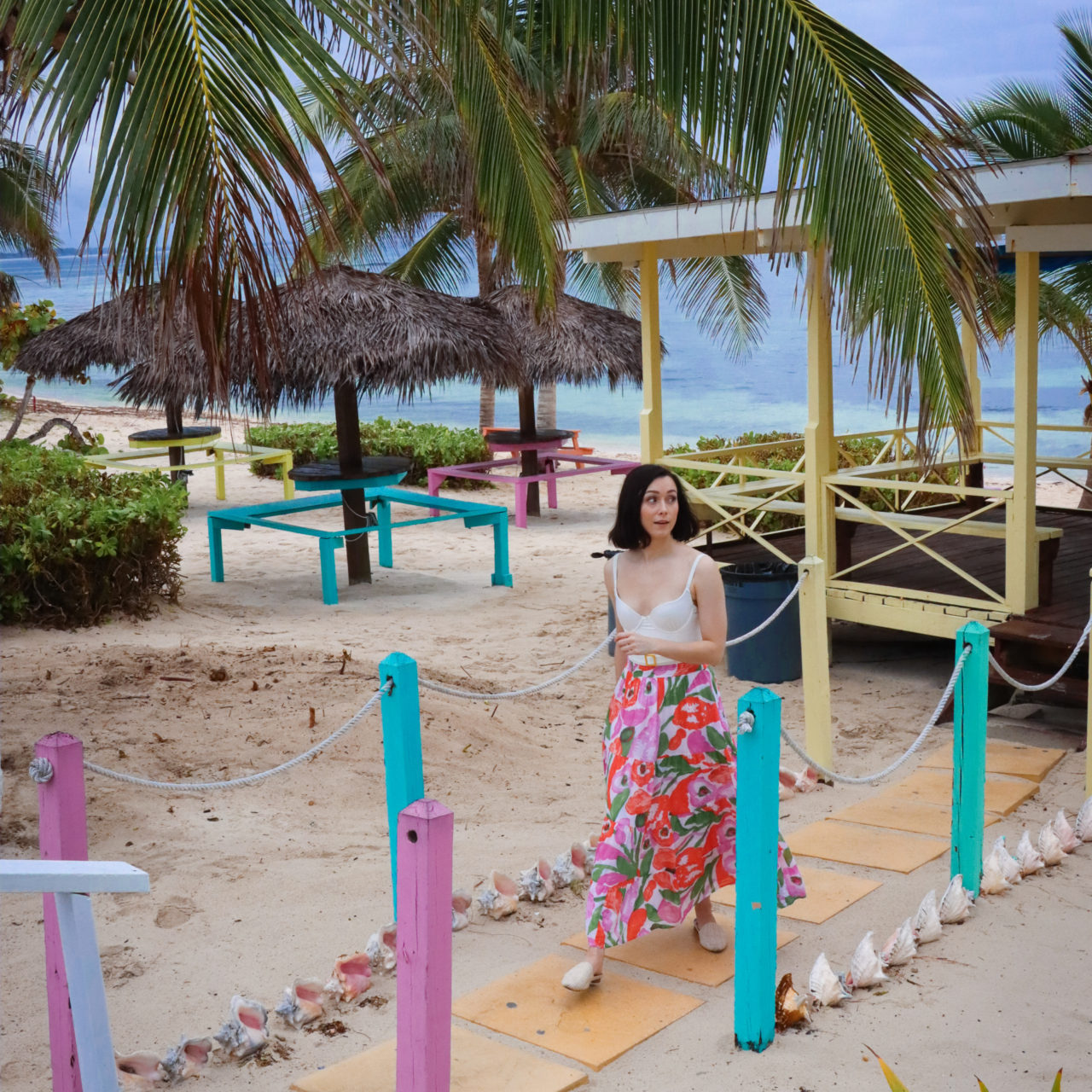 Travel Blogger Jordan Gassner strolling up a colorful walkway in front of Grape Tree Cafe in Cayman Islands