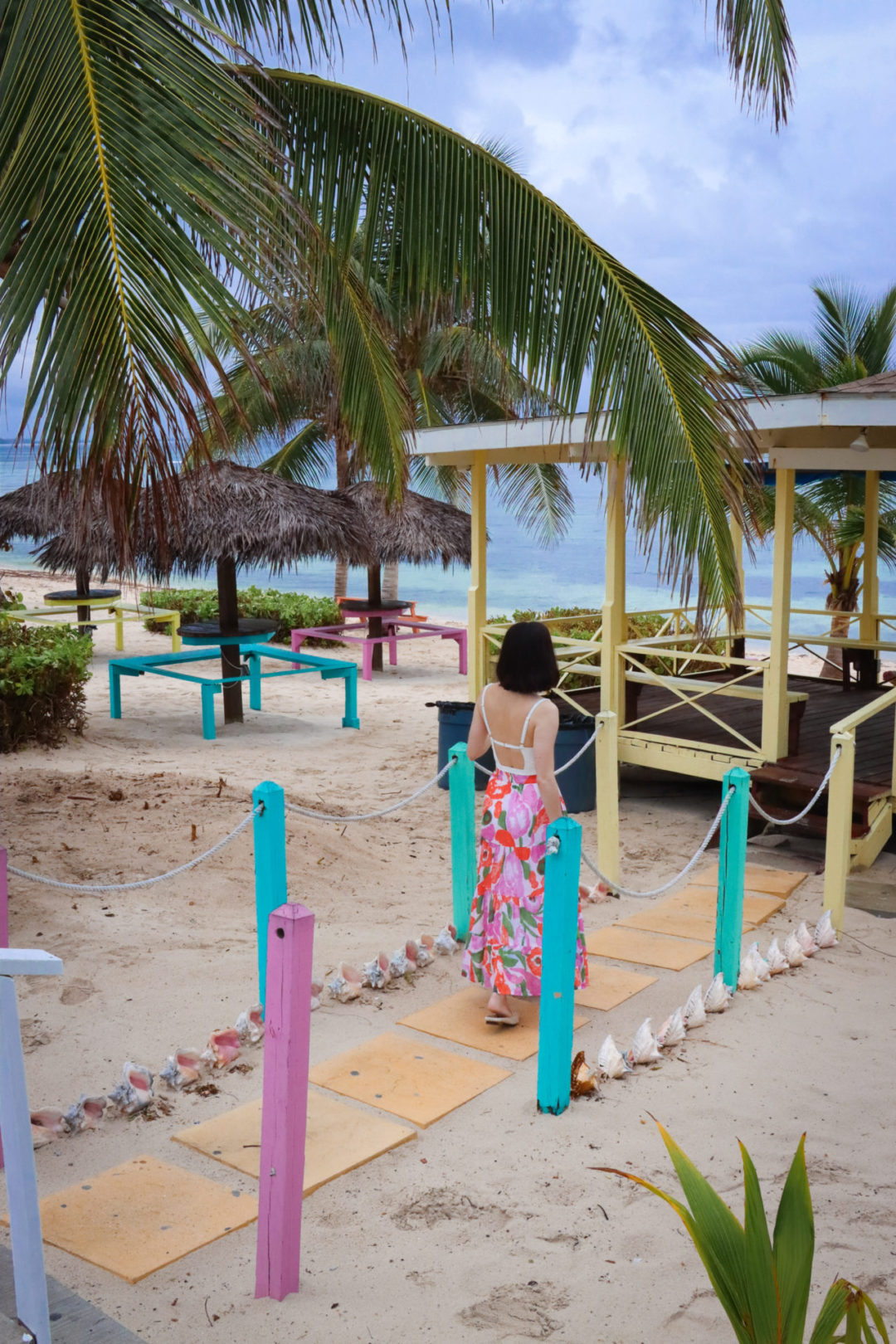 Travel Blogger Jordan Gassner looking toward the ocean on a colorful walkway in front of Grape Tree Cafe in Cayman Islands