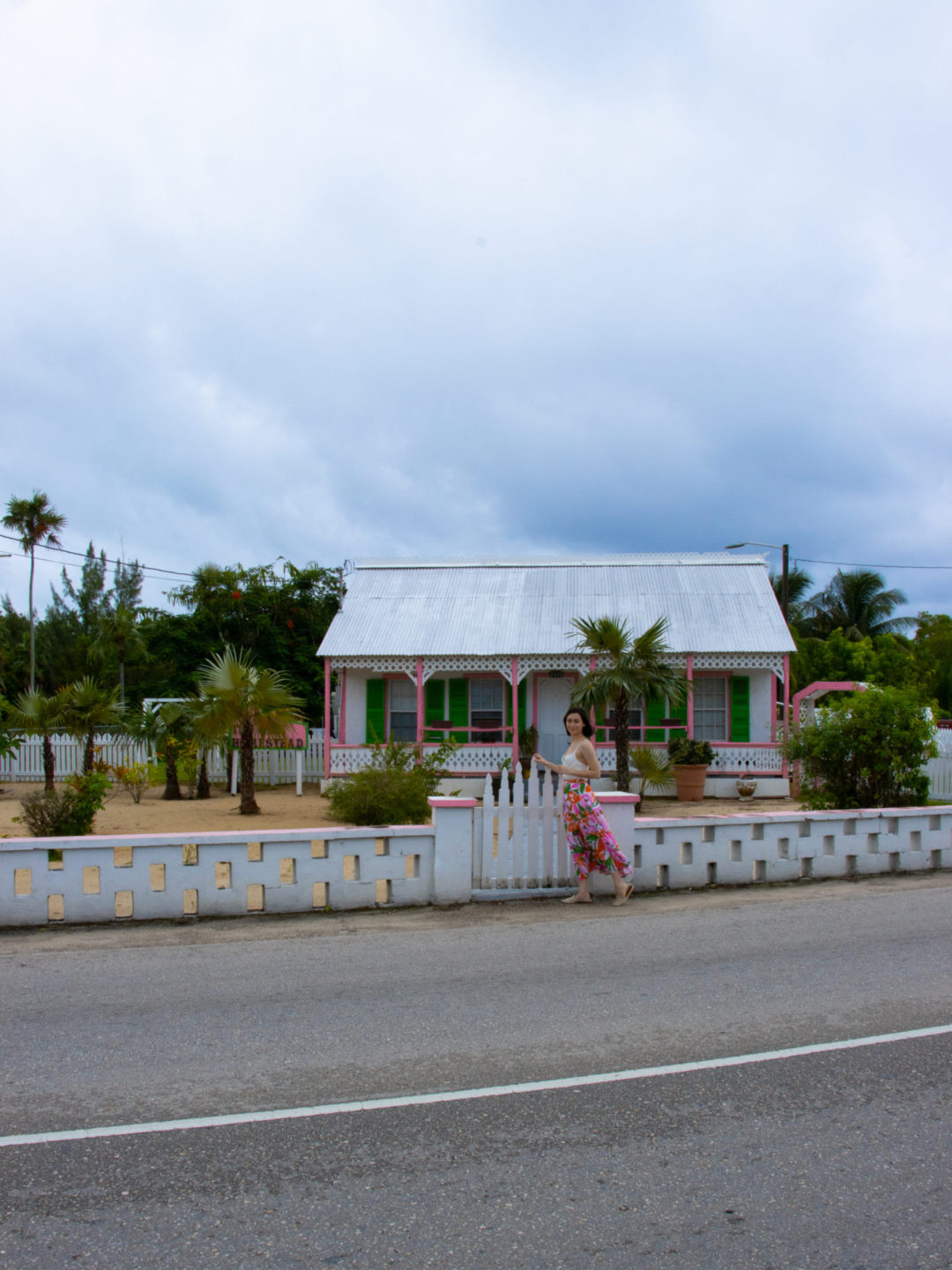 Travel Blogger Jordan Gassner holding onto a white gate in front of a white, pink and green traditional Cayman Islands home