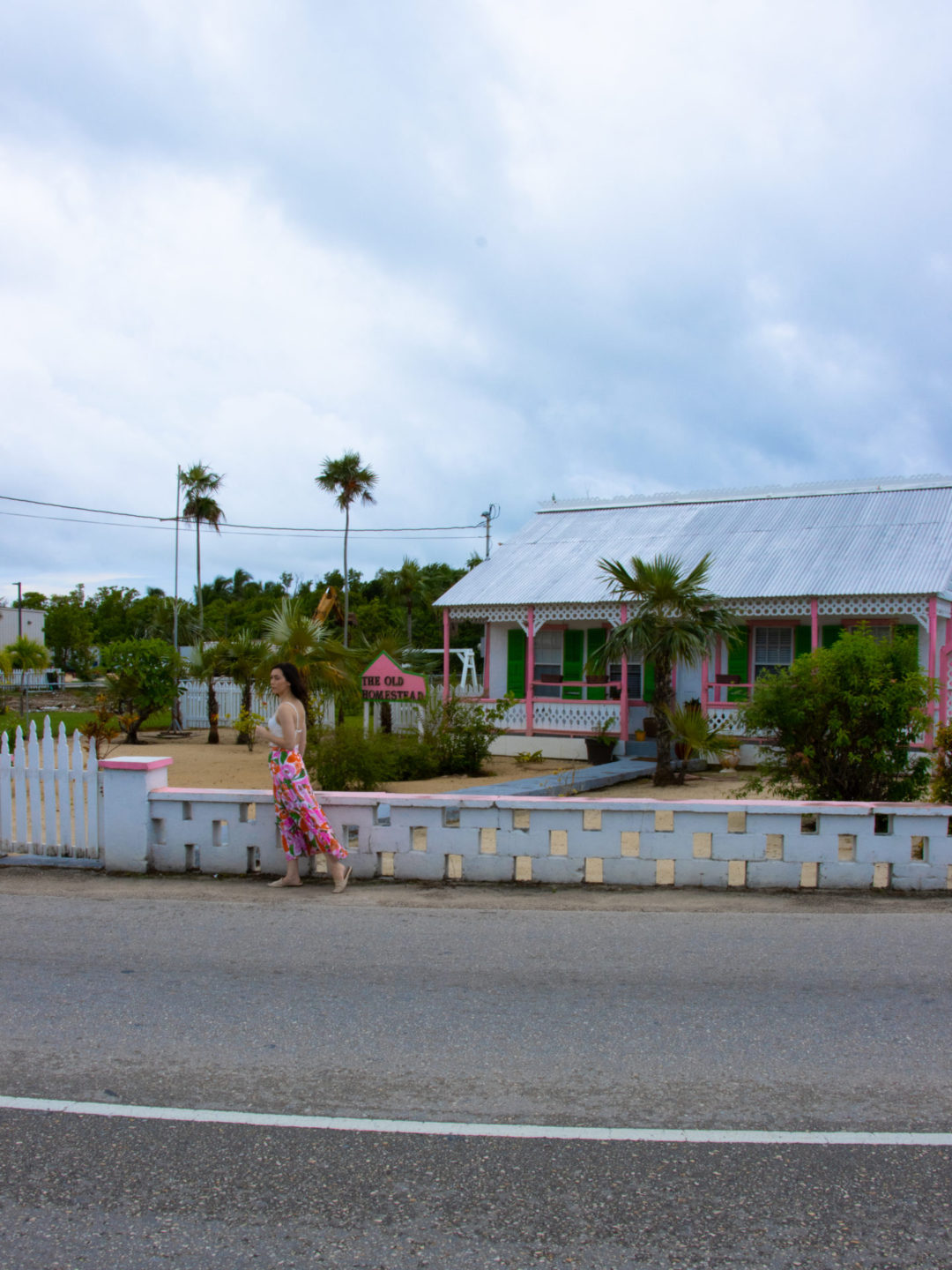 Travel Blogger Jordan Gassner walking along the road in front of a white, pink and green traditional Cayman Islands home