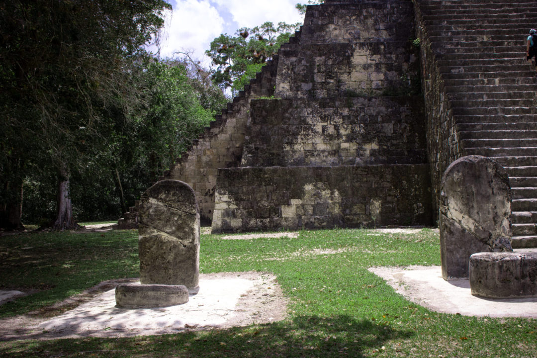 Ruins of Mayan statues in front of a pyramid-like structure inside Guatemala's Tikal National Park