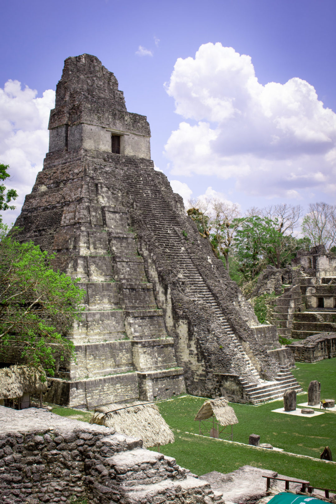 Straw cabanas and rock structures standing at the foot of the giant Templo IV in Tikal National Park