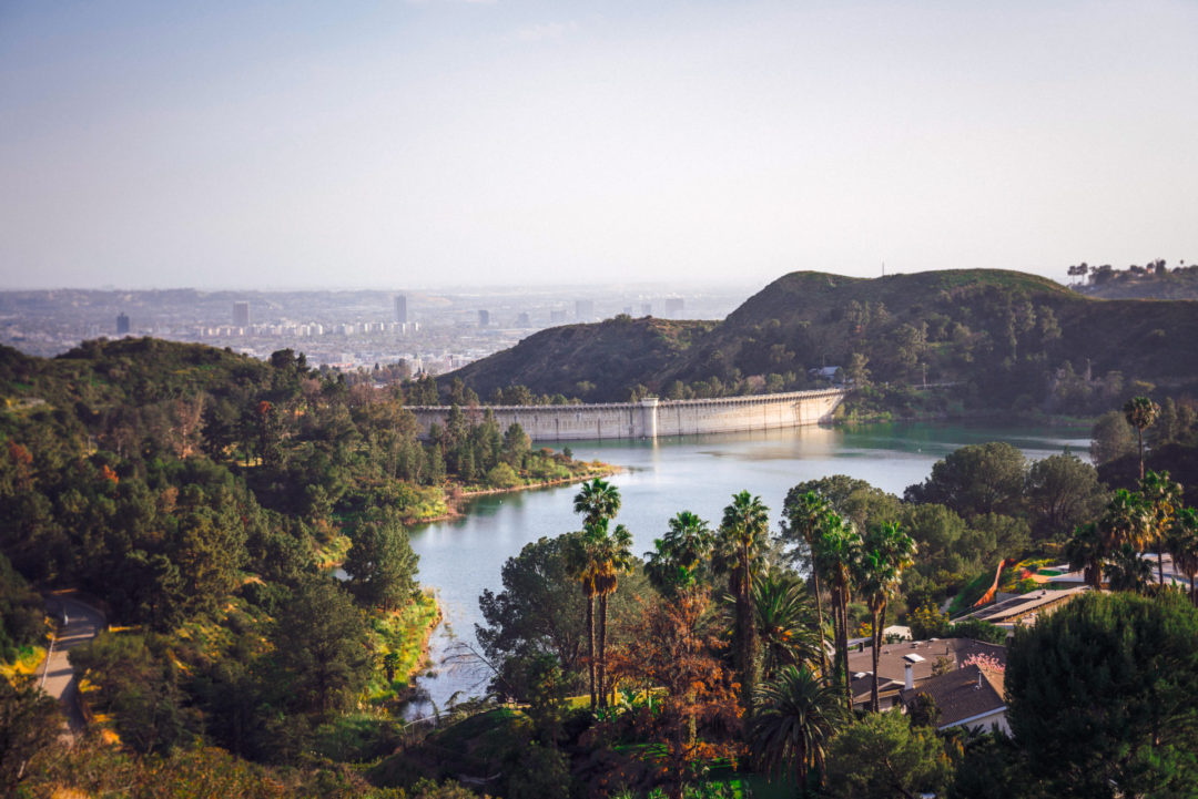 The Hollywood Reservoir surrounded by trees and 1920s architecture overlooking the city of Los Angeles