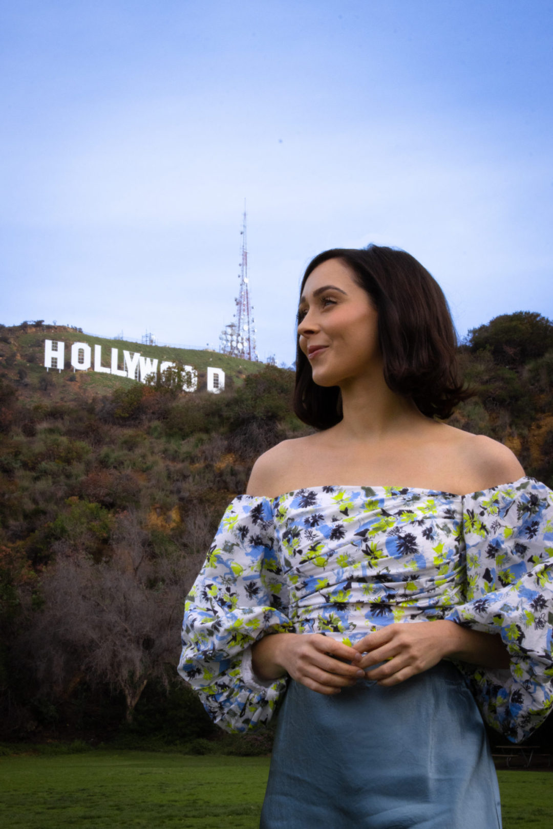 Travel Blogger Jordan Gassner looking to the side in front of a view of the Hollywood Sign at Lake Hollywood Park