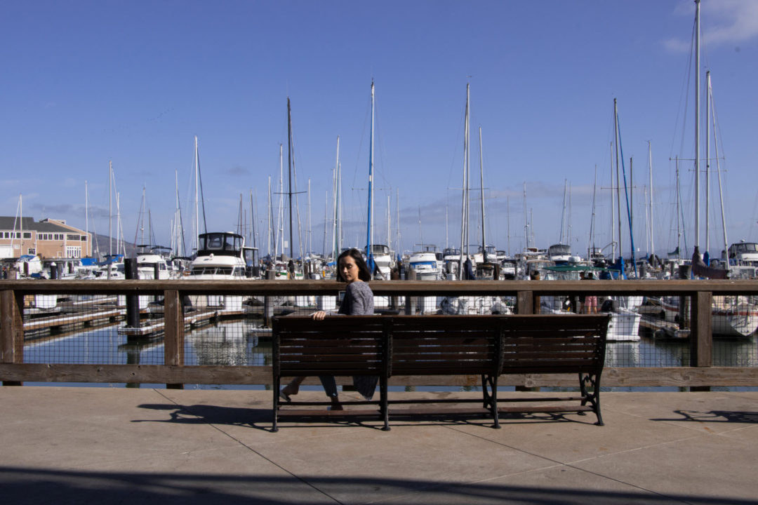 Travel Blogger Jordan Gassner sitting and looking over her shoulder on a bench overlooking the marina at Pier 39 in San Francisco
