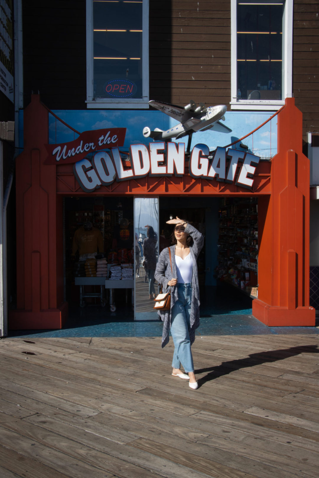 Travel Blogger Jordan Gassner smiling and and shielding her eyes in front of the Under the Golden Gate store at Pier 39 in San Francisco